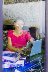 Junge Frau hinter dem Fenster mit Laptop - KNTF000067