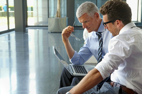 Zwei Geschäftsleute arbeiten an einem Laptop in einer Büro-Lobby, lizenzfreies Stockfoto