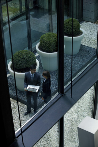 Geschäftsmann und Geschäftsfrau mit Laptop in einem Atrium, lizenzfreies Stockfoto