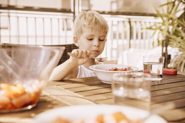 Kleiner Junge sitzt auf dem Balkon und isst Obstsalat - MFF001813