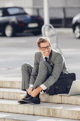 Smiling businessman sitting on steps outdoors tying his shoes - CHAF000421