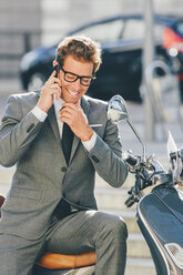 Smiling businessman sitting on motor scooter talking on cell phone - CHAF000551