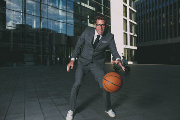 Businessman playing basketball outside office building - CHAF000439