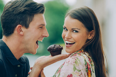 Happy young couple with chocolate muffin outdoors - CHAF000453