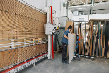 Schreiner in der Werkstatt, der ein Holzbrett aus dem Lager holt - JUBF000023