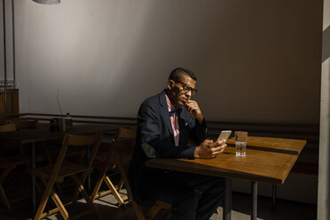 Young man sitting in cafe, waiting for someone, reading text message - CHAF001303