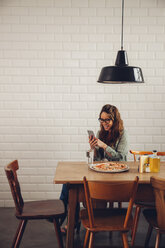 Junge Frau isst Pizza in einem Restaurant und benutzt ein Mobiltelefon - CHAF001280