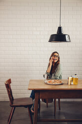 Young woman eating pizza in restaurant, using mobile phone - CHAF001281