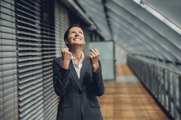 Businesswoman in office building cheering, celebrating success - CHAF000490