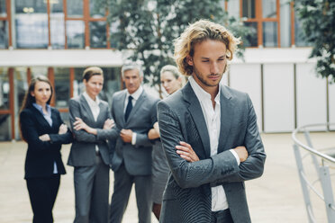 Businessman with crossed arms, excluded from group of business people - CHAF000495