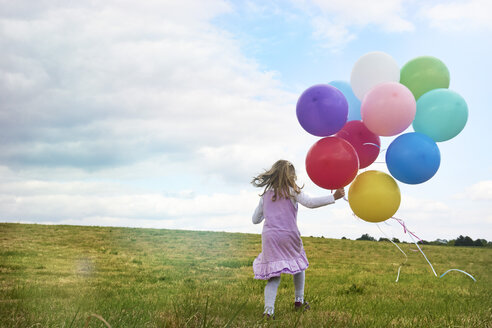 Kleines Mädchen mit Luftballons läuft auf einer Wiese - STKF001317
