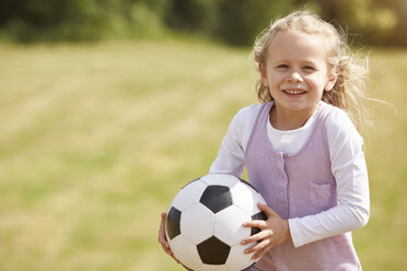 Portrait of smiling little girl with soccer ball on a meadow - STKF001319