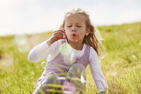 Porträt eines kleinen Mädchens, das auf einer Wiese Seifenblasen bläst, lizenzfreies Stockfoto