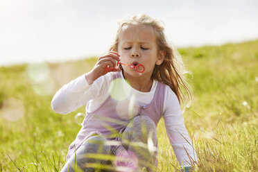 Portrait of little girl blowing soap bubbles on a meadow - STKF001332
