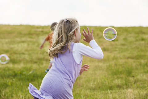 Kleines Mädchen versucht, Seifenblasen auf einer Wiese zu fangen, lizenzfreies Stockfoto