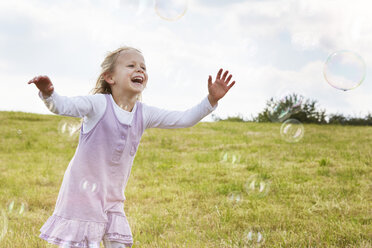 Kleines Mädchen versucht, Seifenblasen auf einer Wiese zu fangen - STKF001336