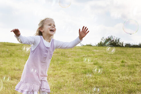 Little girl trying to catch soap bubbles on a meadow - STKF001336