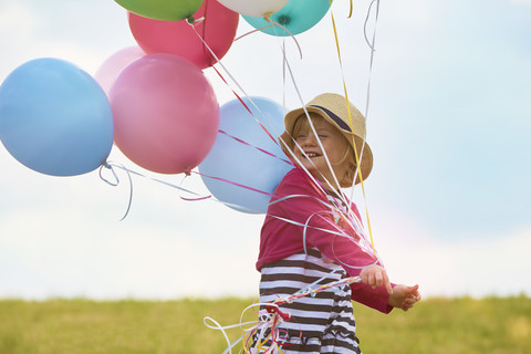 Kleines Mädchen mit Luftballons auf einer Wiese, lizenzfreies Stockfoto