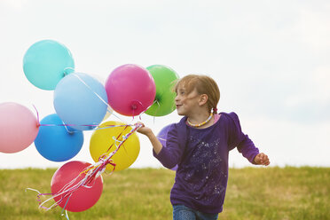 Kleines Mädchen mit Luftballons läuft auf einer Wiese - STKF001351
