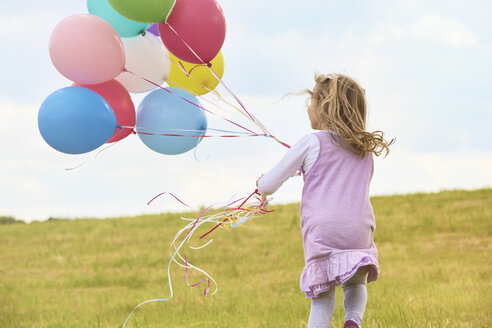 Kleines Mädchen mit Luftballons läuft auf einer Wiese - STKF001353