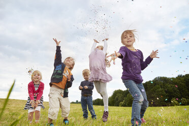 Fünf kleine Kinder, die auf einer Wiese Konfetti werfen - STKF001357