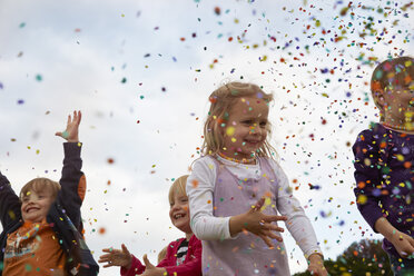 Vier kleine Kinder, die auf einer Wiese Konfetti werfen - STKF001358