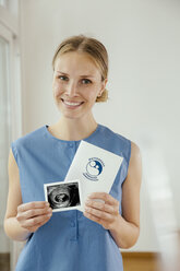 Smiling young woman holding ultrasound image and maternity log - MFF001843