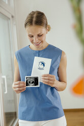Smiling young woman holding ultrasound image and maternity log - MFF001844