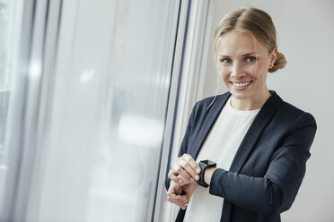 Lächelnde junge Geschäftsfrau, die ihre Smartwatch überprüft - MFF001854