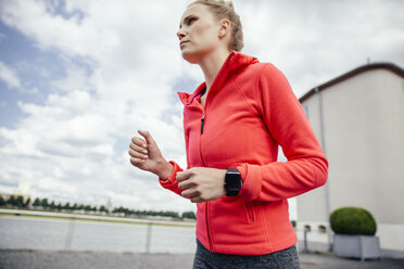 Deutschland, Köln, junge Frau beim Joggen mit Smartwatch - MFF001861