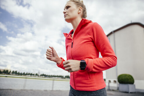 Deutschland, Köln, junge Frau beim Joggen mit Smartwatch - MFF001861