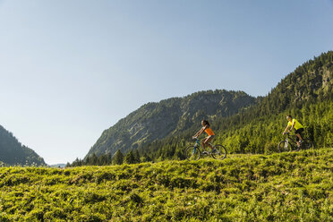 Österreich, Tirol, Tannheimer Tal, junges Paar auf Mountainbikes in alpiner Landschaft - UUF004930