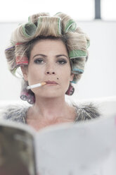 Porträt einer Frau mit Lockenwicklern und Zeitschrift, die eine Zigarette raucht - ZEF006297