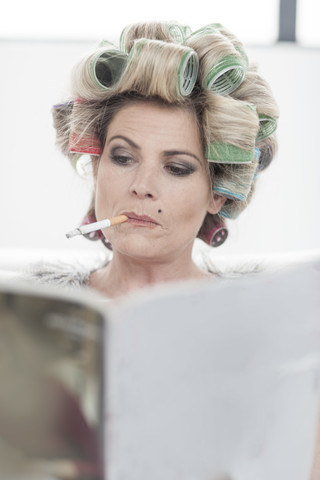 Portrait of woman with hair curlers and magazine smoking a cigarette stock photo