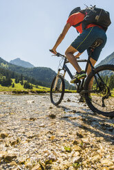 Österreich, Tirol, Tannheimer Tal, junger Mann auf Mountainbike beim Überqueren eines Baches - UUF004951