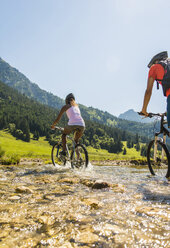 Österreich, Tirol, Tannheimer Tal, junges Paar auf Mountainbikes beim Überqueren eines Baches - UUF004952