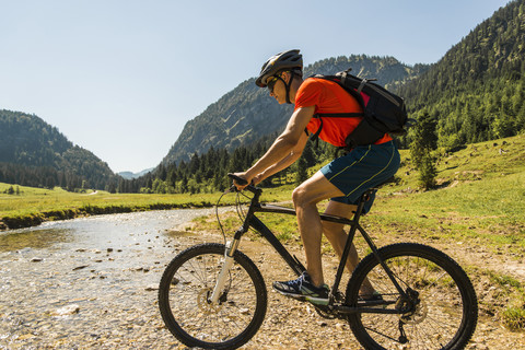 Austria, Tyrol, Tannheim Valley, young man on mountain bike crossing brook stock photo