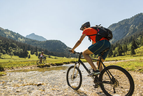 Österreich, Tirol, Tannheimer Tal, junger Mann auf Mountainbike beim Überqueren eines Baches - UUF004954