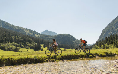 Österreich, Tirol, Tannheimer Tal, junges Paar fährt Mountainbike am Flussufer - UUF004955