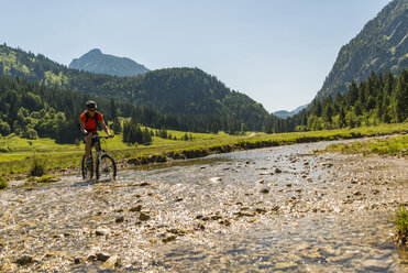 Österreich, Tirol, Tannheimer Tal, junger Mann auf Mountainbike beim Überqueren eines Baches - UUF004957