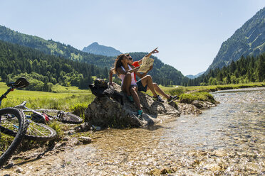 Austria, Tyrol, Tannheim Valley, young couple with mountain bikes and map sitting at brook - UUF004960