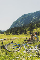 Österreich, Tirol, Tannheimer Tal, junges Paar mit Mountainbikes auf einer Wiese - UUF004982