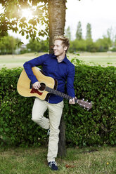 Lächelnder junger Mann spielt Gitarre im Park - GDF000795