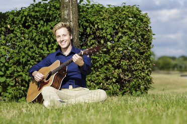 Lächelnder junger Mann spielt Gitarre auf einer Wiese - GDF000796