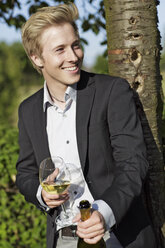 Lächelnder junger Mann im Freien mit Weinglas und Flasche - GDF000807