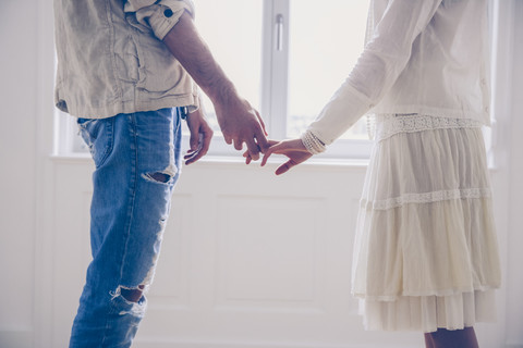 Mittelteil eines Paares, das Hand in Hand am Fenster steht, lizenzfreies Stockfoto