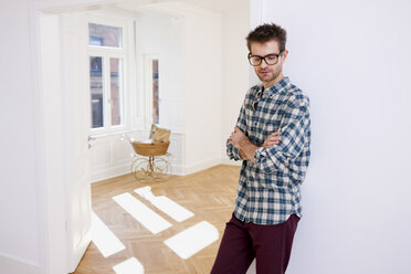 Thoughtful young man standing in new home with pram in background - CHAF000583