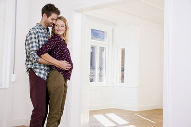 Young man embracing pregnant woman in new home - CHAF000588