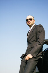 Porträt eines Geschäftsmannes mit Sonnenbrille, der sich an einem Auto lehnt - ABZF000089