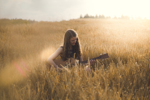 Junge Frau spielt abends auf einem Feld Gitarre, lizenzfreies Stockfoto